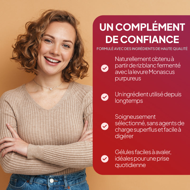Une femme souriante aux cheveux bruns bouclés se tient debout devant un fond beige chaleureux ; elle porte un pull beige à côtes et un jean bleu. À sa droite se trouve un grand panneau publicitaire rouge comportant un texte en français sur un complément alimentaire, avec notamment la mention « UN COMPLÈMENT DE CONFIANCE » et des puces accompagnées de coches.