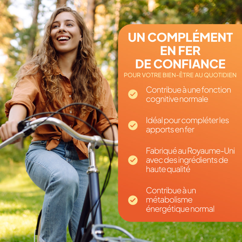 Une femme souriante qui fait du vélo en plein air sur un chemin herbeux, avec à droite un grand panneau orange comportant un texte en français faisant la promotion d'un complément alimentaire à base de fer destiné à renforcer la confiance.